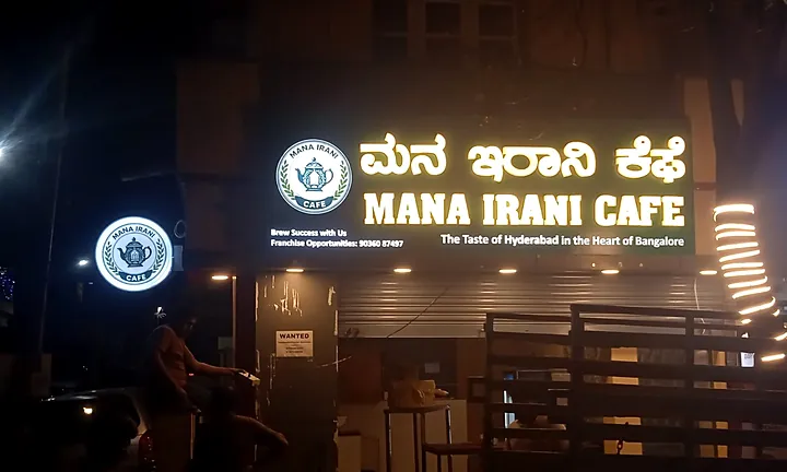 Mana Irani Cafe at night with lit white letters and round logo sign