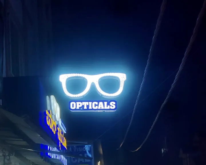 Glasses-shaped LED sign for an optical shop glowing over a busy street at night
