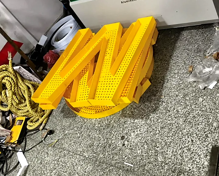 A perforated yellow channel letter M next to the letter-bending machine